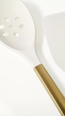 Elegant kitchen utensils including a slotted spoon with a gold handle on a light background.