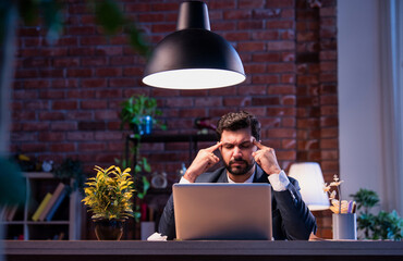 Indian businessman at desk holding head in pain, suffering from stress and workplace burnout
