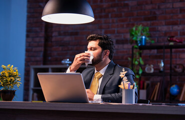 Indian businessman sneezing coughing at desk, shows signs of seasonal illness during office work