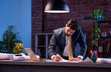Asian architect working on technical drawing and blueprint at office desk with focused expression