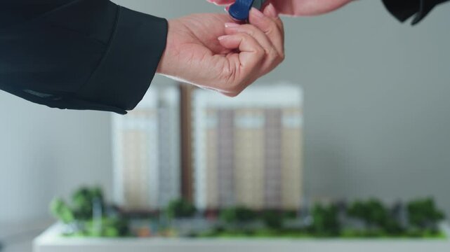 close up moment of hand stretched forward to receive key symbolizing property handover or new ownership with blurred background of building miniature enhancing context of real estate transaction