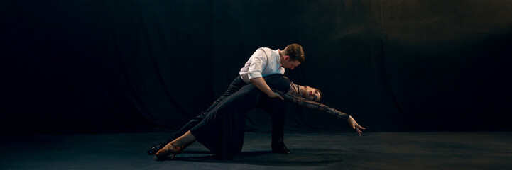 Argentine tango dancers hold a dramatic pose against a dark stage backdrop. Concept of an intense performance and the expression of cultural dance. Banner