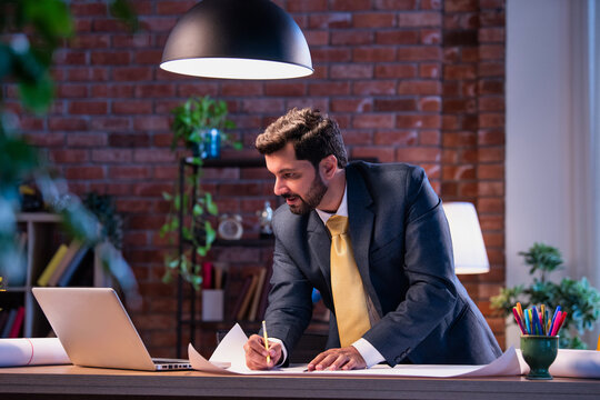 Asian architect working on technical drawing and blueprint at office desk with focused expression