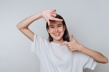 Young asian woman making framing gesture with hands against plain background while smiling and...