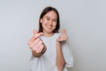 Smiling asian young woman making heart gesture with hands indoors against plain backdrop