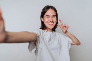 Smiling young woman poses for a selfie while making a peace sign in a bright studio