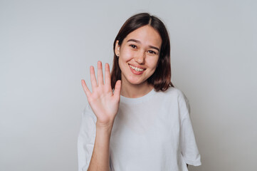 Smiling asian young woman waving hand in a light-colored room during daytime