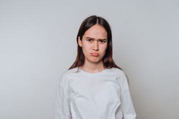 Young woman expressing disappointment in a neutral setting during daytime with a light-colored...