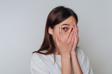 Young woman expresses surprise and emotion while hiding her face with her hands in a neutral setting