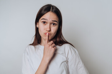 Young asian woman with finger on lips making silent gesture in minimalist indoor setting
