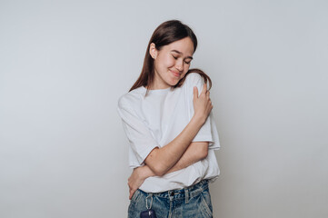 Woman embracing herself with a warm smile in a simple indoor setting