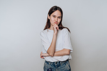 Young asian woman poses thoughtfully with one hand on her chin in a simple studio setting