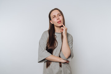 Thoughtful young woman pondering an idea with a playful expression against a light background