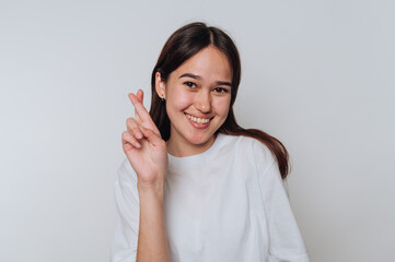 Young asian woman smiling and crossing her fingers for good luck in a bright indoor setting during...