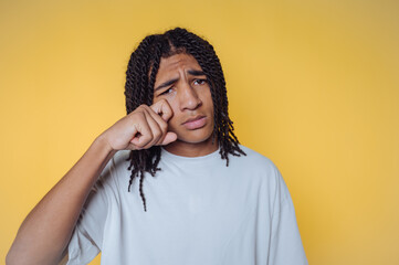 Young man with braided hair shows a thoughtful expression against a bright yellow background in a...