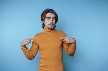Young man wearing a turtleneck sweater poses confidently against a solid blue background while...