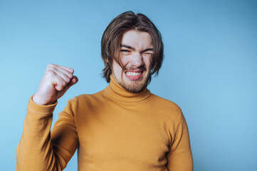 Young man expressing victory with clenched fist against a light blue background during a cheerful...