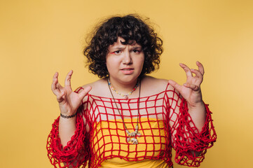 Woman wearing a red netted top against a yellow background shows an expressive pose with her hands...
