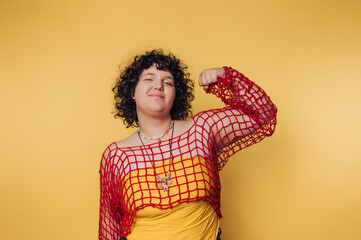 Confident young woman strikes a pose against a vibrant yellow background while wearing a colorful...