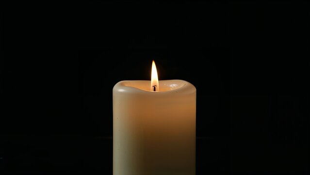 Burning steadily, ivory pillar candle casting warm glow in dark studio, with black background