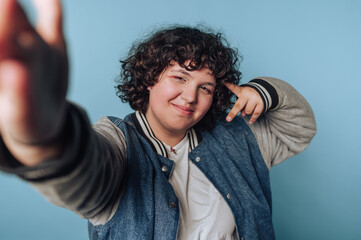 Teenager posing confidently against a light blue backdrop, showcasing playful spirit with a peace...