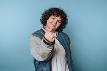 Young person expressing affection with hand gesture against a blue background in a casual setting