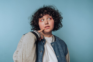 Young person in a denim jacket poses thoughtfully against a blue background