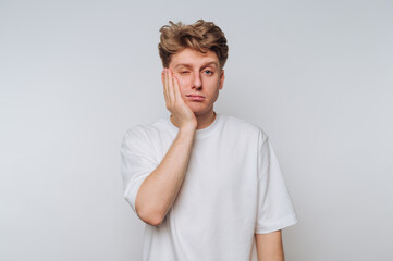 Young man expressing frustration while touching his face against a plain background in a casual...
