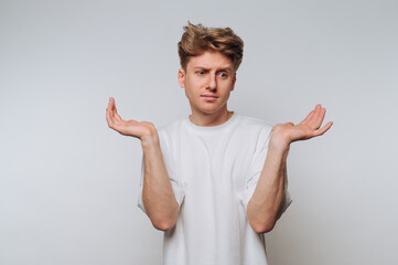 Confused young man expressing uncertainty while standing against a white background