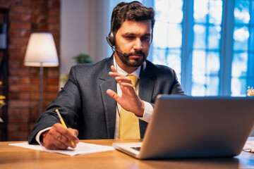 Indian businessman writes notes during online call, showing focus, learning, and remote teamwork