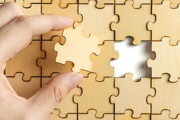 hand holding wooden jigsaw puzzle pieces. To complete the puzzle. business and teamwork concept.