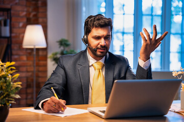 Indian businessman writes notes during online call, showing focus, learning, and remote teamwork