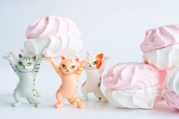 Funny toy kittens lift a pink-and-white marshmallow treat together in a playful delivery concept on a clean white background. Photo