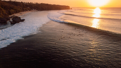 Surfers on Padang Padang surfspot at sunset with perfect swell waves