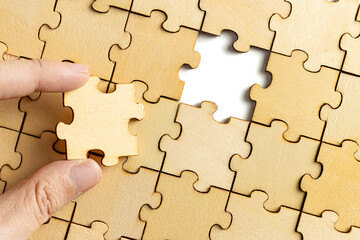 hand holding wooden jigsaw puzzle pieces. To complete the puzzle. business and teamwork concept.
