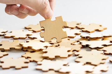 hand holding a wooden jigsaw puzzle pieces. with scattered puzzle pieces in background.