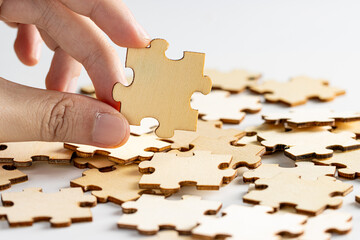 hand holding a wooden jigsaw puzzle pieces. with scattered puzzle pieces in background.