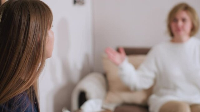 Side view of specialist with long hair taking notes while engaged in thoughtful conversation with patient seated in background, hand raised in expressive gesture during calm therapy session