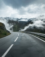 Left curve at empty mountain road in Swiss alps. Driving down ice-covered alpine pass on cloudy...