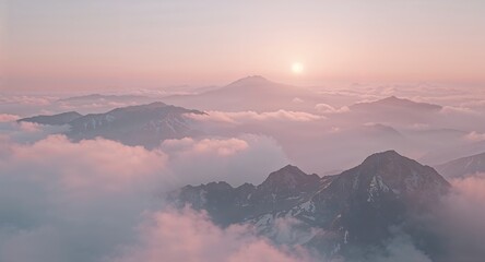 Fototapeta premium Aerial view of mountain peaks emerging from a sea of clouds under a soft pink sunrise sky above the horizon
