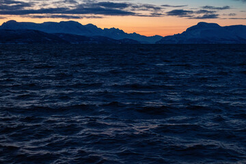 Rare sunrise glow over icy fjords and the quiet Norwegian Sea during the polar night in Norway.