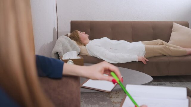 Guest reclines on comfortable sofa with eyes closed during emotional dialogue with attentive listener holding green pen and notebook in relaxed therapeutic setting promoting mental clarity