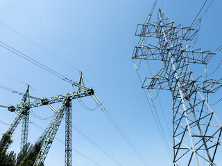Electric power transmission towers with high-voltage lines against clear blue sky, metal lattice...