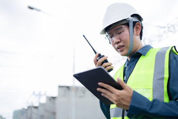 Engineer is working at high voltage power substation using tablet and walkie talkie for inspection and check of electrical infrastructure ensuring safety and efficiency