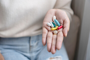 Close-up of a woman’s hand holding various pills, capsules, and vitamins, showing daily health care, supplement use, or the risk of taking too much medicine