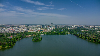 Naklejka premium Wide drone shot of Herastrau Lake with city skyline, modern office buildings, and lush urban forest