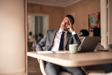 Businessman Reflecting At Desk with Coffee and Laptop in Modern Office Setting