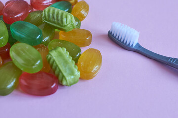 Colorful candies and a toothbrush on a pink background.