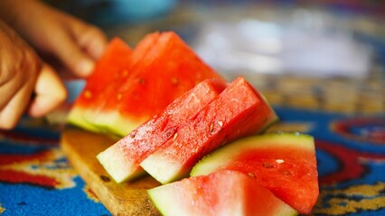 A close-up of hands slicing a juicy red watermelon on a wooden cutting board, highlighting the...