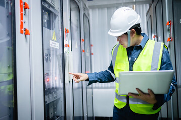 Electrical engineer in safety helmet and vest performs inspection with control panel inside...